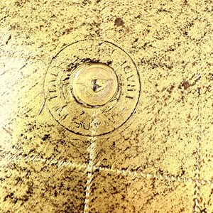 May include: Close-up of a gold-colored metal surface with a circular inscription that reads "THAILAND 1938".