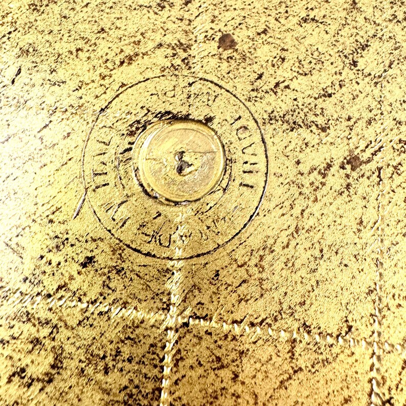 May include: Close-up of a gold-colored metal surface with a circular inscription that reads "THAILAND 1938".