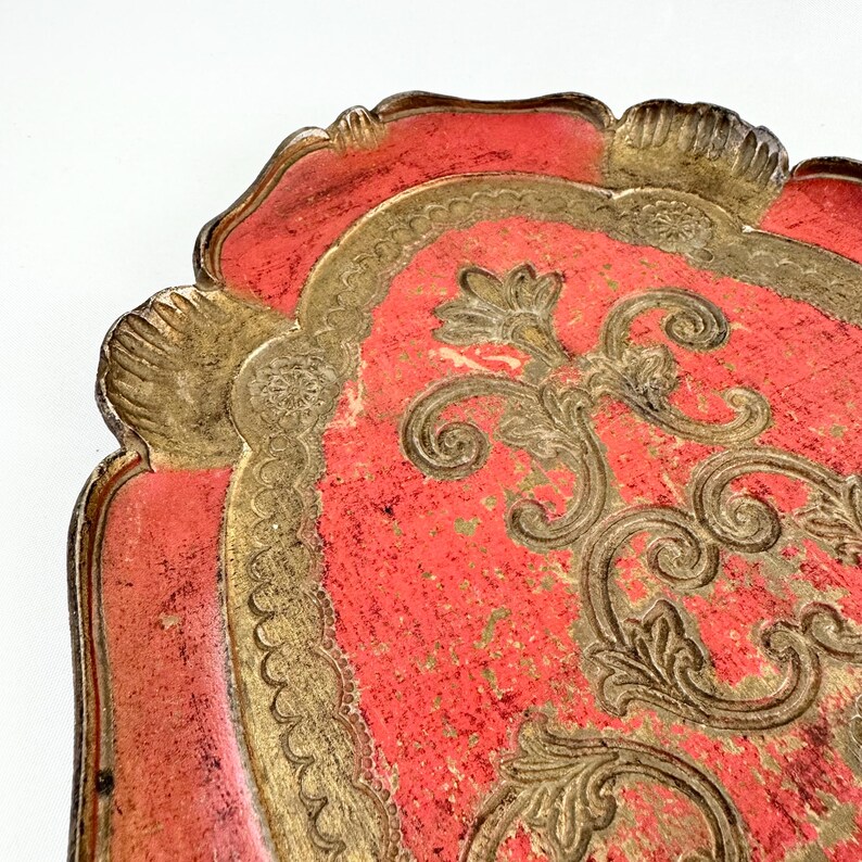 May include: A vintage red and gold tray with a decorative floral design. The tray has a scalloped edge and is made of wood.