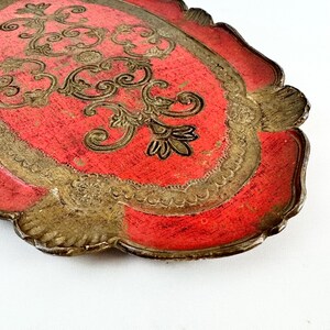 May include: A red and gold oval tray with a decorative floral design. The tray has a scalloped edge and is made of wood.