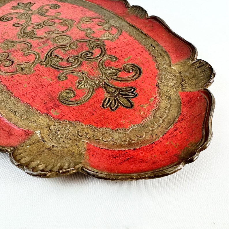 May include: A red and gold oval tray with a decorative floral design. The tray has a scalloped edge and is made of wood.