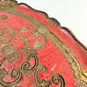 May include: A red and gold decorative tray with an ornate design. The tray has a scalloped edge and is made of wood.