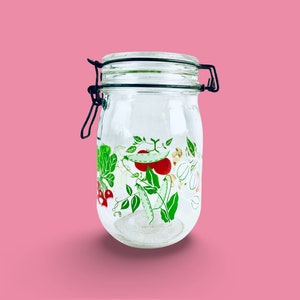 May include: A clear glass jar with a black metal lid and a green and red vegetable design. The jar is empty.