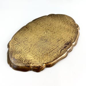 May include: A gold-colored oval tray with a decorative scalloped edge. The tray has a textured surface and a slightly raised center.