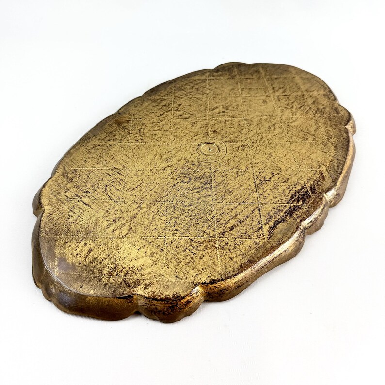 May include: A gold-colored oval tray with a decorative scalloped edge. The tray has a textured surface and a slightly raised center.