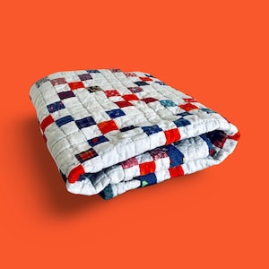 Peut inclure: Une courtepointe patchwork pliée avec un fond blanc et des carrés de tissu rouge, bleu et blanc.
