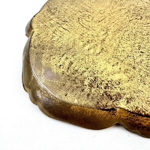 May include: A gold-colored metal tray with a scalloped edge. The tray has a distressed finish, giving it a vintage look.
