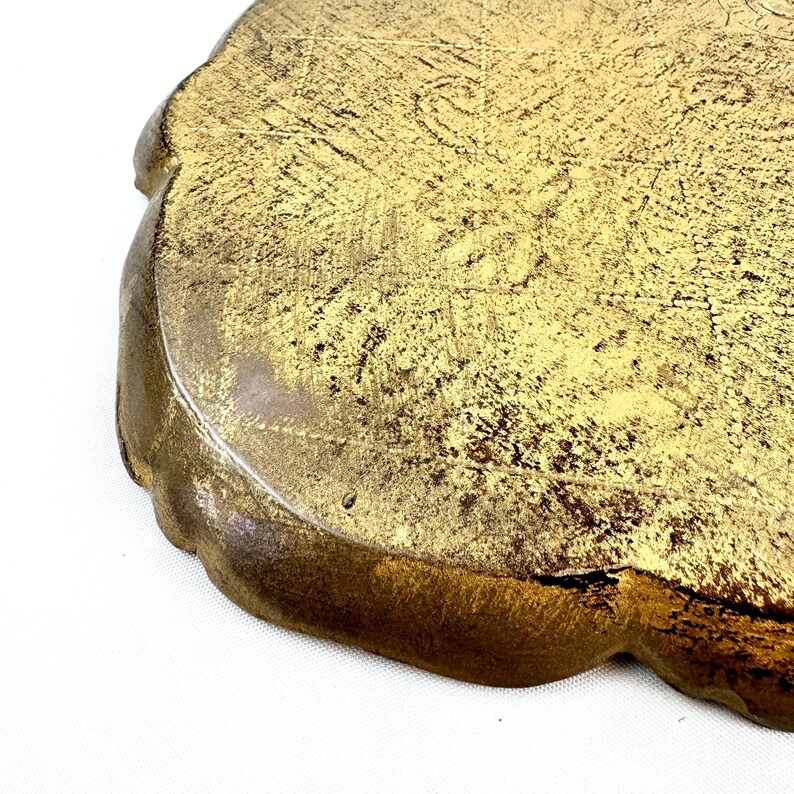 May include: A gold-colored metal tray with a scalloped edge. The tray has a distressed finish, giving it a vintage look.