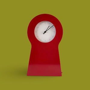 May include: A red clock with a white face and black hands. The clock is shaped like a keyhole.
