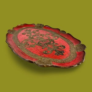 May include: An oval-shaped red tray with a gold-colored design. The tray has a scalloped edge and a raised rim.