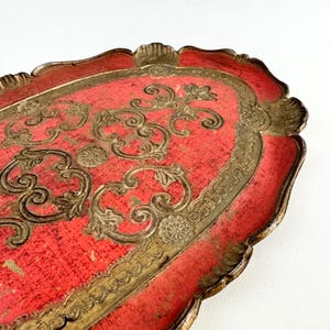 May include: A red and gold oval serving tray with a decorative floral design. The tray has a scalloped edge and is made of wood.