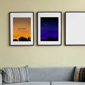 May include: Three framed prints on a wall, the leftmost print has a sunset cityscape with the text "NOT INCLUDED" in the sky, the middle print has a dark blue sky with a crescent moon, and the rightmost print is blank.