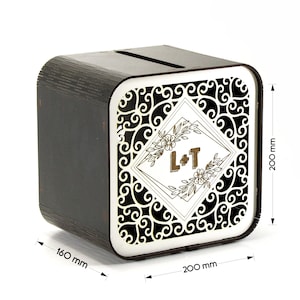 Könnte beinhalten: Dunkelbraune Holzbox mit Schlitz oben. Die Frontplatte hat ein weißes, verziertes Design mit goldenen Initialen "L+T". Die Box ist 20 cm breit, 20 cm hoch und 16 cm tief. Ideal für Hochzeiten oder besondere Anlässe.