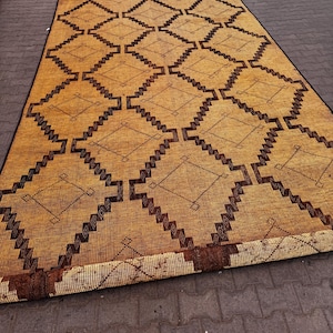 Puede incluir: Una alfombra rectangular tejida con un patrón geométrico de diamantes en tonos marrones y beige. La alfombra está enrollada en la parte inferior, revelando la parte inferior. La alfombra está hecha de fibras naturales y es adecuada para uso en interiores o exteriores.