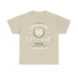 May include: A beige t-shirt with a gold graphic that says "LEBENDE 50 JAHRE JUNG LEGENDE Thomas PREMIUM QUALITAT MADE IN GERMANY 50 JAHRE ZUR PERFENTION GERIEFT"