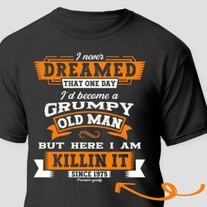 Könnte beinhalten: Schwarzes T-Shirt mit einer orangefarbenen Grafik, auf der steht: "Ich habe nie davon geträumt, dass ich eines Tages ein grantiger alter Mann werden würde, aber hier bin ich und rocke es seit 1975. Premiumqualität."