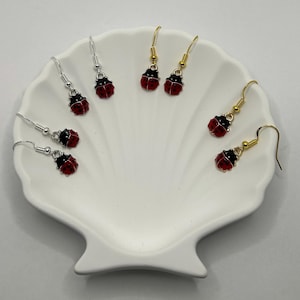 May include: Three pairs of ladybug earrings, each pair featuring a different colour of metal: silver, gold, and rose gold. The ladybugs are red with black spots.