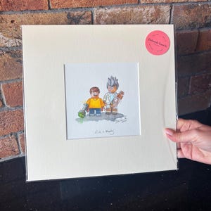 May include: A watercolor painting of Rick and Morty from the animated series Rick and Morty, depicted as Lego minifigures. The painting is framed in a white mat and a white frame. The artist's signature and the year 2023 are visible in the bottom right corner of the painting. The title "Rick + Morty" is written below the painting.