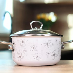 Può includere: Una pentola di smalto bianco con un coperchio di vetro e manici argentati. La pentola ha un motivo floreale.