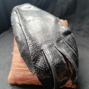 Peut inclure: Un gant noir présentant un motif texturé semblable à des écailles sur toute sa surface. Le gant possède des sections pour les doigts distinctes et une bordure sombre et lisse, mettant en valeur un motif géométrique détaillé.