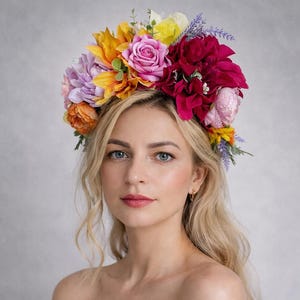 May include: A woman wearing a colourful floral crown with yellow, orange, pink, and purple flowers. She is wearing an off-the-shoulder dress with a floral pattern. The background is a soft grey.