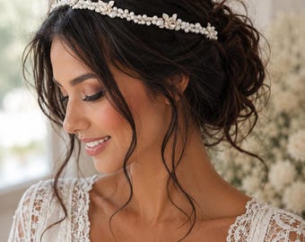May include: A delicate bridal headband featuring a series of small, round pearls and floral accents. The headpiece is silver-toned and worn on dark hair. The woman is wearing a white lace dress.