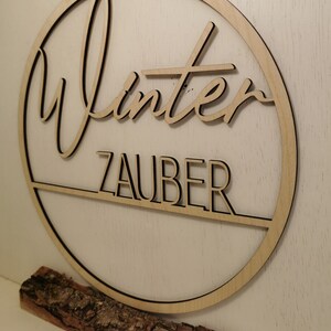Pu&ograve; includere: Un cerchio di legno con la scritta "Winterzauber" su di esso. Il cerchio &egrave; su una base di legno.