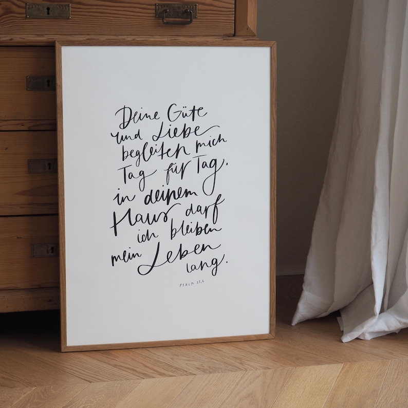 May include: A framed print with German text in black script on a white background. The wooden frame is light brown. The text includes the words "Deine G&uuml;te und Liebe begleiten mich Tag f&uuml;r Tag".