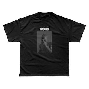 May include: Black t-shirt with a white graphic of a person's face with the word "blond" printed above the image.