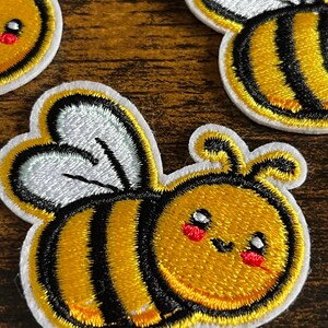 May include: Three embroidered iron-on patches of cute cartoon bees with black and yellow stripes, white wings, and red cheeks.