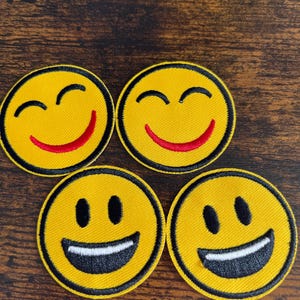 May include: Four yellow embroidered smiley face patches with black outlines. Two of the smiley faces have red smiling mouths and closed eyes. The other two smiley faces have white smiling mouths and black eyes.