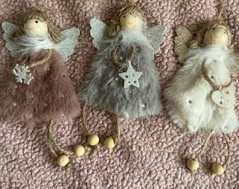 Puede incluir: Tres adornos de ángel decorativos con alas brillantes, cuerpos esponjosos y cabezas de madera. Cada ángel tiene un cuerpo de diferente color: malva, gris y blanco. Cuelgan de hilo con cuentas de madera y son perfectos para la decoración navideña.