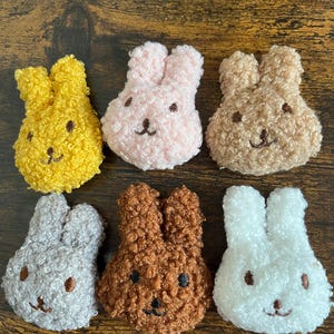 May include: Six plush bunny toys in different colours, including yellow, pink, brown, grey, brown, and white. The bunnies have embroidered faces with black eyes and noses.