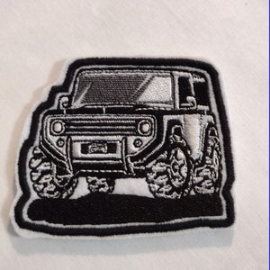 Könnte beinhalten: Schwarz-weiß gestickter Aufnäher einer Jeep mit schwarzem Hintergrund. Der Jeep hat einen weißen Kühlergrill und Scheinwerfer.