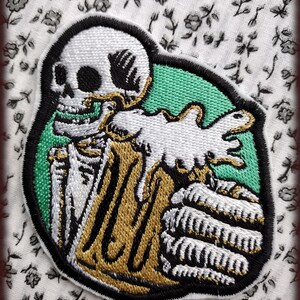 May include: Embroidered patch featuring a skeleton holding a stack of gold coins. The skeleton is white with black outlines, and the coins are gold with black outlines. The background is a green circle.