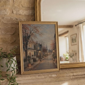 Puede incluir: Una l&aacute;mina de arte mural rectangular enmarcada que muestra una escena callejera durante el oto&ntilde;o. La imagen representa casas con ventanas iluminadas, &aacute;rboles con follaje naranja, farolas y calabazas a lo largo de una acera.