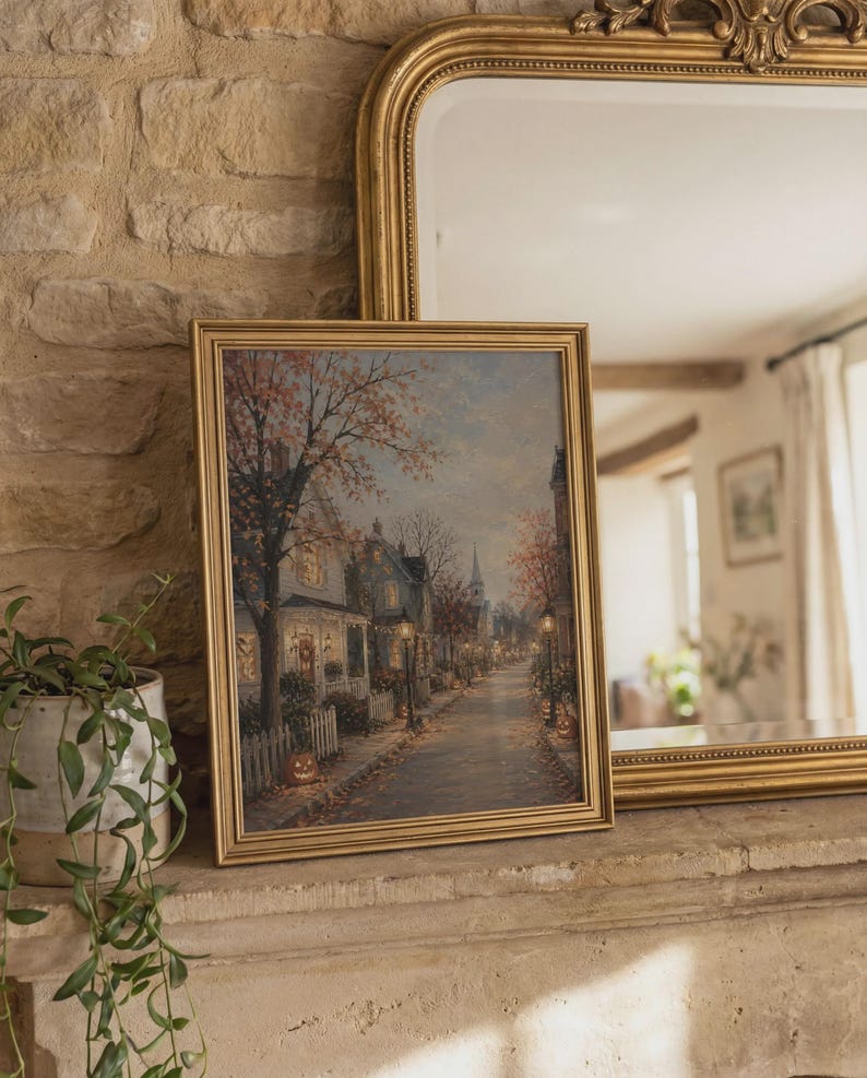 Puede incluir: Una l&aacute;mina de arte mural rectangular enmarcada que muestra una escena callejera durante el oto&ntilde;o. La imagen representa casas con ventanas iluminadas, &aacute;rboles con follaje naranja, farolas y calabazas a lo largo de una acera.