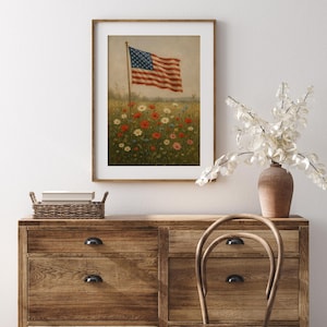 May include: Framed print of the American flag waving in a field of wildflowers. The artwork features a vintage style with a wooden frame. The flag has red and white stripes and a blue field with white stars. The flowers are red, white, and yellow.
