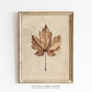 May include: A framed vintage print featuring a detailed, dried maple leaf in shades of brown and tan. The leaf is centered on a beige background, within a distressed, light-colored wooden frame. The text "DIGITALLY DRAWN PRINTS Vintage Printable Wall Art" is at the bottom.