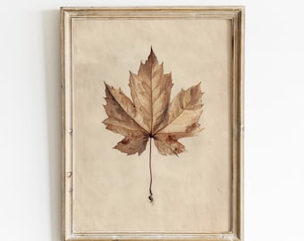 May include: A framed vintage print featuring a detailed, dried maple leaf in shades of brown and tan. The leaf is centered on a beige background, within a distressed, light-colored wooden frame. The text "DIGITALLY DRAWN PRINTS Vintage Printable Wall Art" is at the bottom.