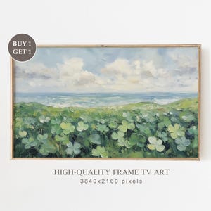 May include: A framed landscape painting of a coastal scene. The artwork shows a field of green clovers, rolling hills, a blue ocean, and a cloudy sky. The frame is a light brown colour. Text on the image reads "BUY 1 GET 1" and "HIGH-QUALITY FRAME TV ART".