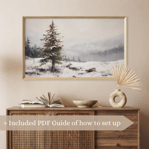 May include: A framed watercolor painting of a snowy forest scene with a single pine tree in the foreground. The painting has a light blue and gray color scheme and a soft, dreamy feel.