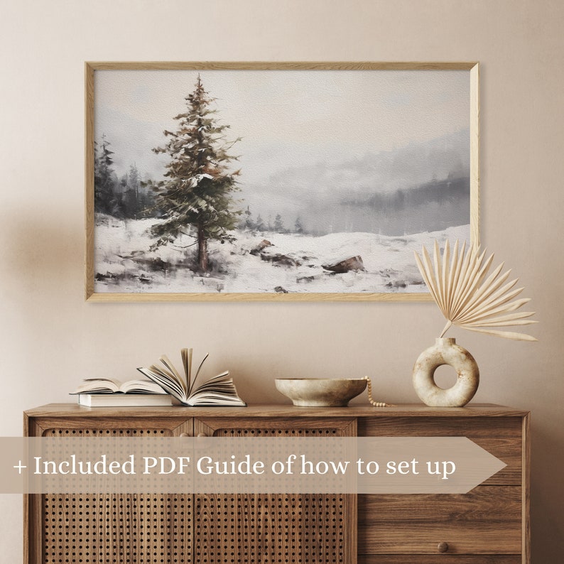May include: A framed watercolor painting of a snowy forest scene with a single pine tree in the foreground. The painting has a light blue and gray color scheme and a soft, dreamy feel.