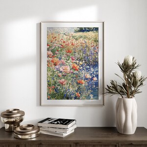 Pode incluir: Uma pintura em aquarela emoldurada de um campo de flores silvestres em tons de rosa, vermelho e azul. As flores est&atilde;o dispostas em uma fileira, com um riacho de &aacute;gua atravessando o centro da imagem.