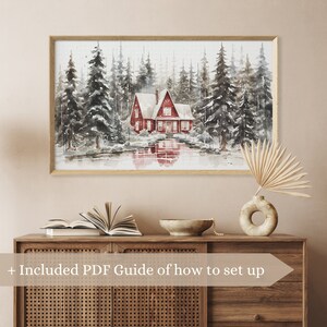 May include: A watercolor painting of a red cabin in a snowy forest. The cabin has a white roof and is surrounded by tall, snow-covered trees. The painting is framed in a light wood frame.