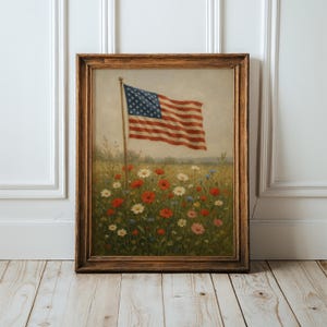 May include: Framed artwork featuring an American flag waving above a field of wildflowers. The flag has red and white stripes and a blue canton with white stars. The flowers are red, white, and blue, with a brown wooden frame.