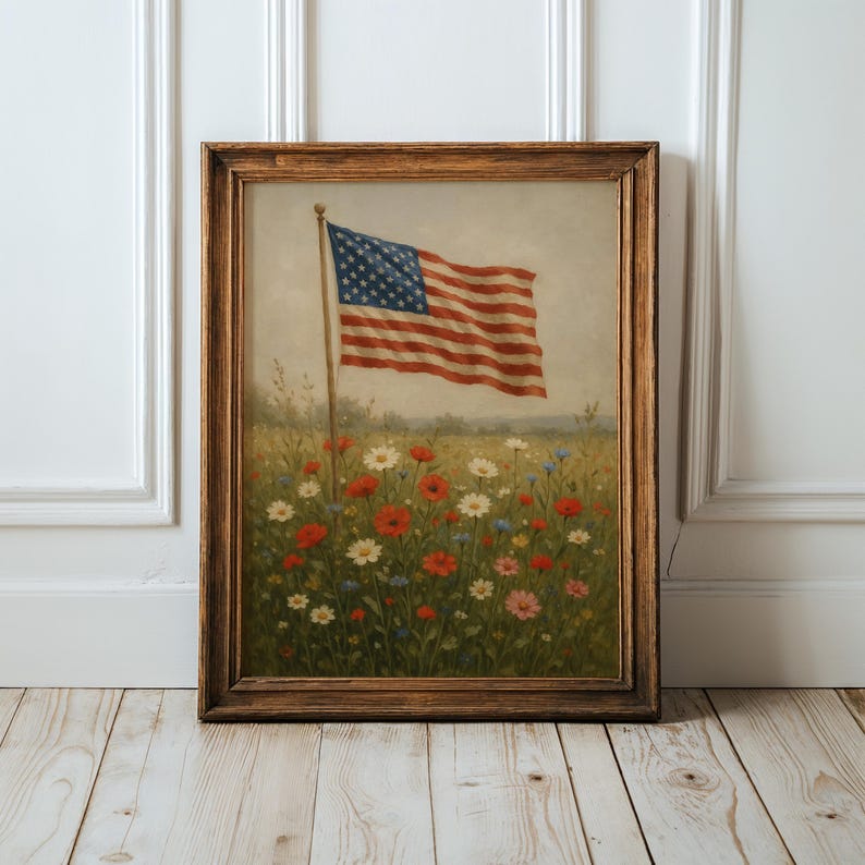 May include: Framed artwork featuring an American flag waving above a field of wildflowers. The flag has red and white stripes and a blue canton with white stars. The flowers are red, white, and blue, with a brown wooden frame.