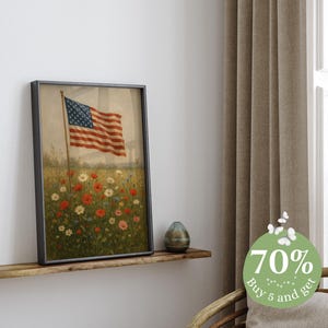 May include: Framed print of the American flag waving in a field of wildflowers. The artwork features a vintage aesthetic with a black frame. The flag has red and white stripes and a blue field of stars. The flowers are red, white, and yellow.
