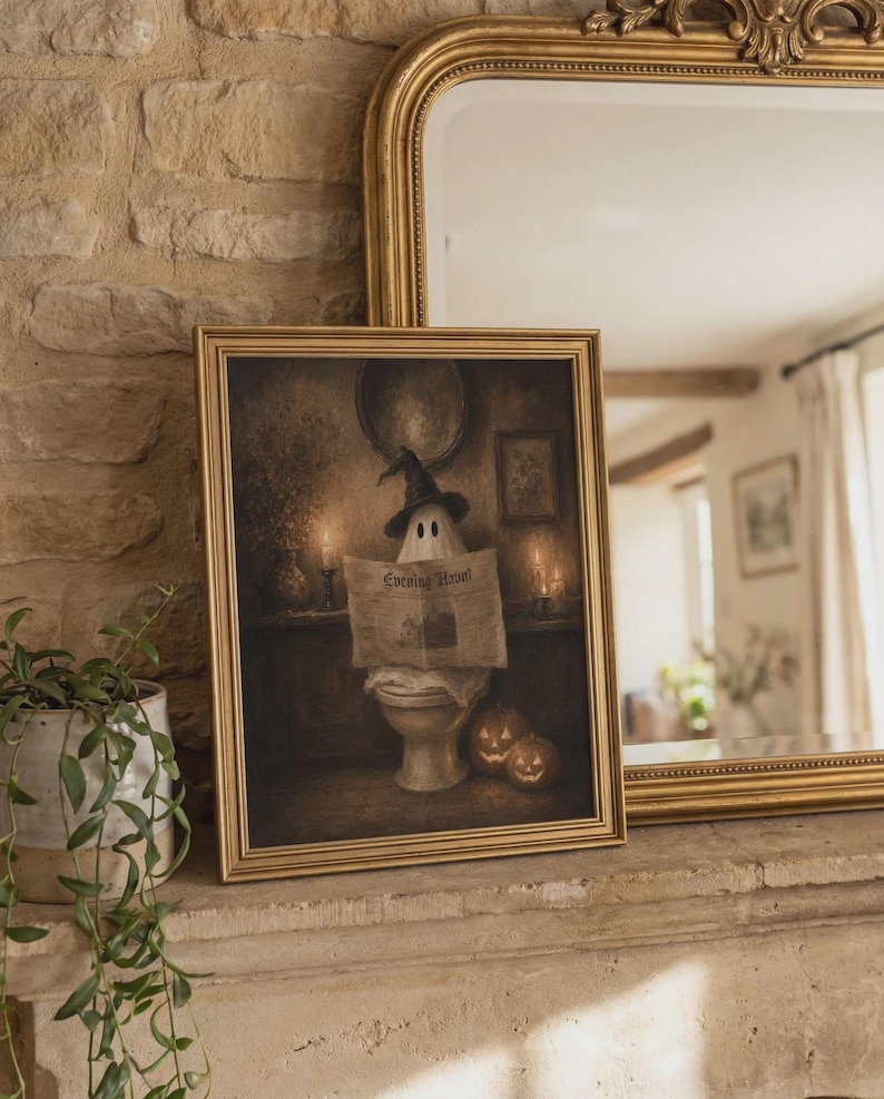 May include: A framed wall art print featuring a ghost wearing a black witch hat, sitting on a toilet while reading a newspaper titled Evening Howl. Two lit jack-o'-lanterns sit on the floor beside the ghost in a dimly lit, moody interior setting.