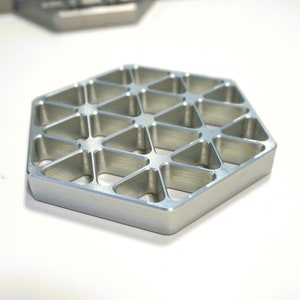 May include: A silver hexagonal metal coaster with a geometric pattern of small triangles. The coaster has a brushed finish.